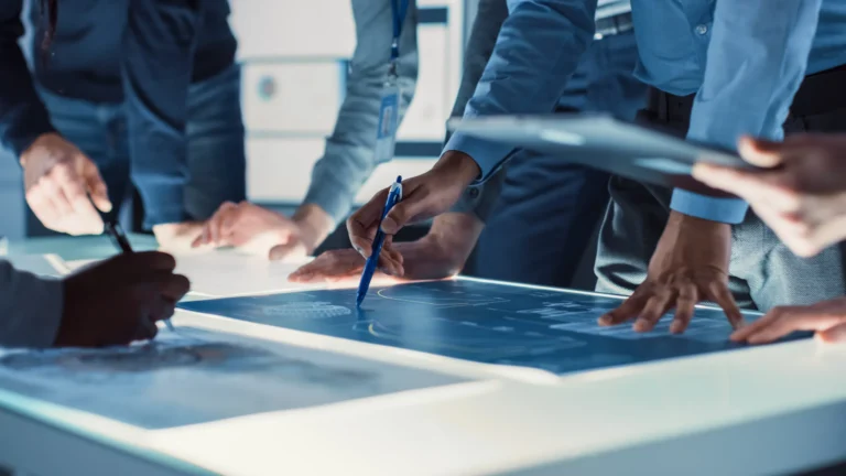 Engineers gathered around a work table, marking up blue structural drawings with a pen while designing a building.