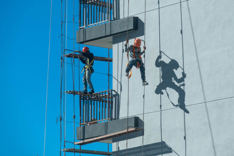 Two rope-access technicians suspended along the glass facade of a high-rise building for a facade inspection (Bill 122).