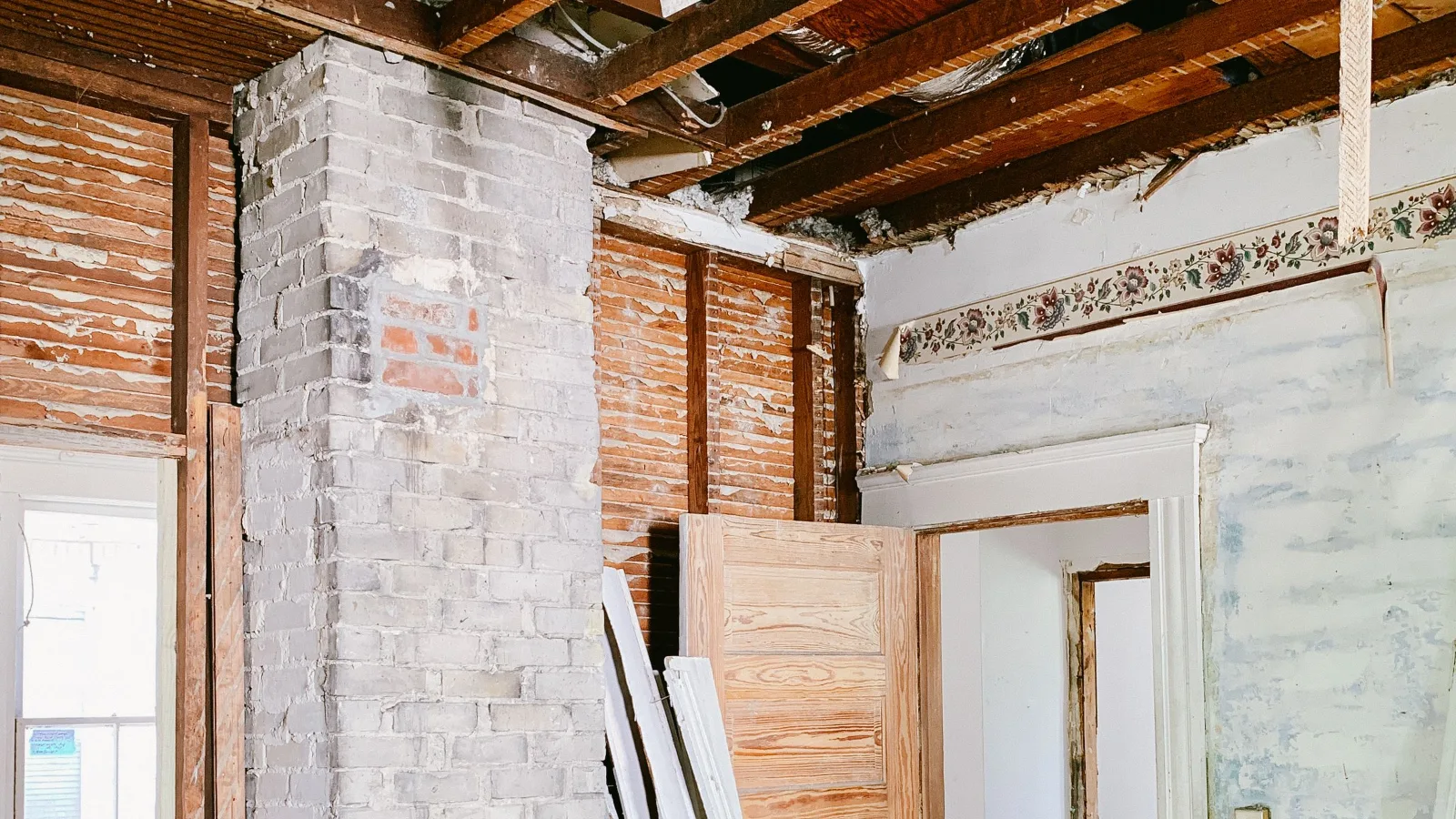 Plafond ouvert laissant voir les solives de bois d’une maison ancienne en rénovation, à côté d’une cheminée de brique