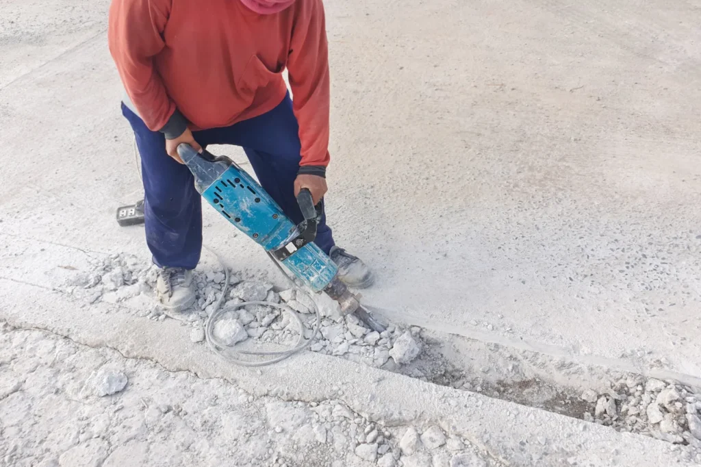 Ouvrier qui démolit une dalle de béton au marteau-piqueur avant le retrait du remblai pyriteux